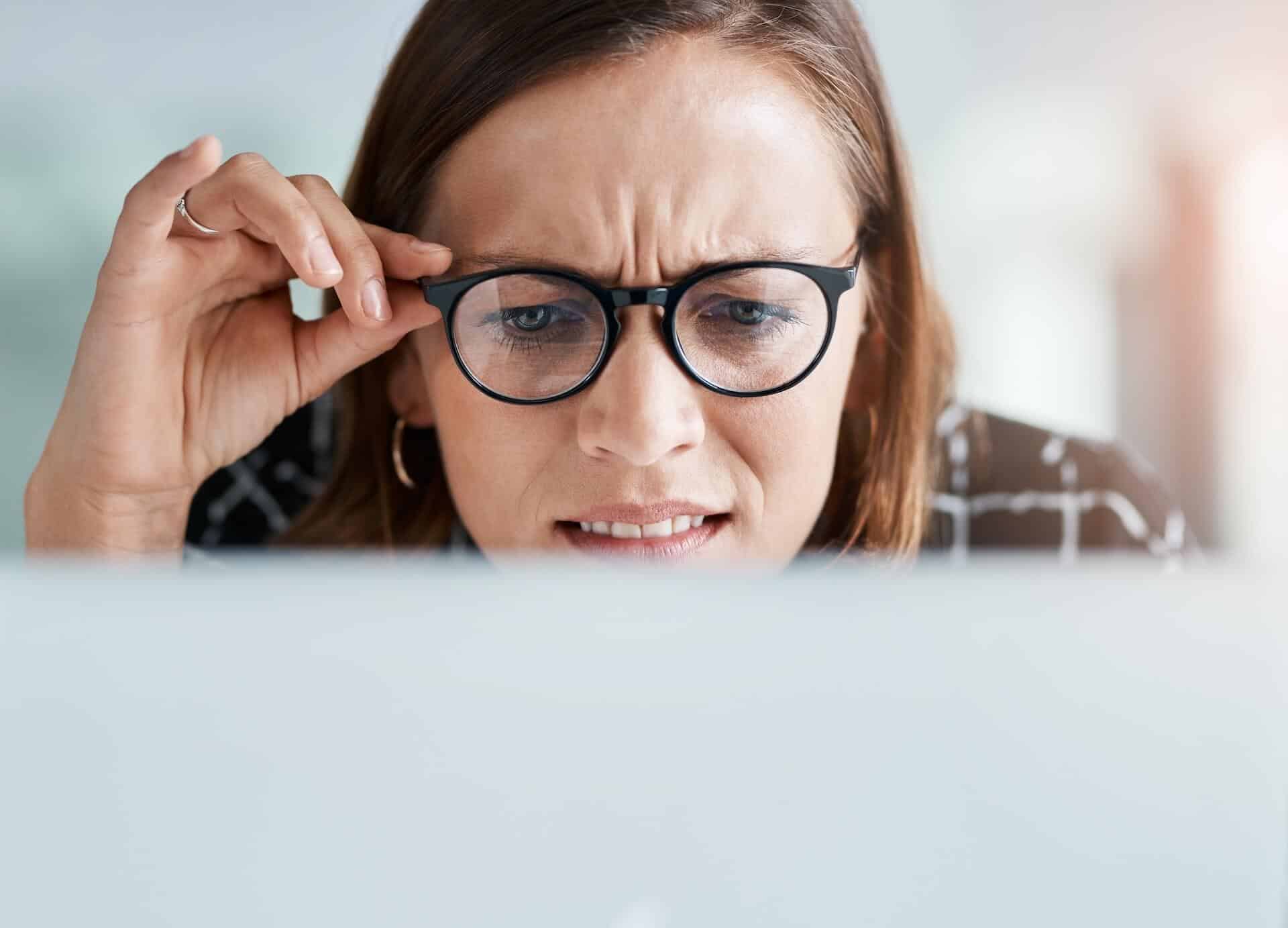 woman holding glasses staring at computer